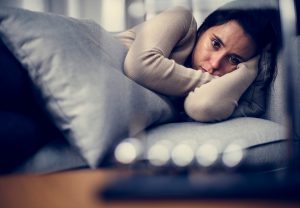 An individual lying on a sofa wrapped in a comforter, looking withdrawn and depressed.